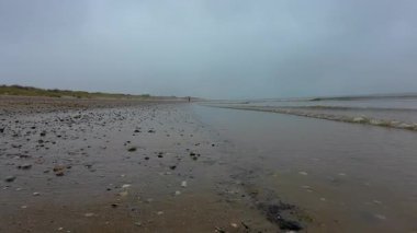 Sakin bir sahil manzarası, yumuşak su ve gri gökyüzünün altında pürüzsüz çakıl taşları, dingin ruh halleri için mükemmel ve kaçış için.