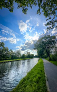 Güzel ve manzaralı nehir kenarı yolu yemyeşil yeşilliklerle ve yukarıda parlak mavi gökyüzüyle kaplı.