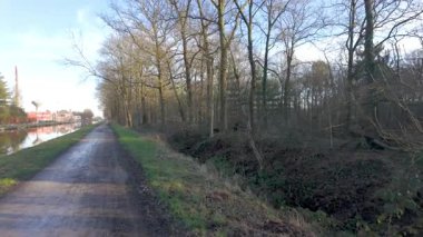 Huzurlu bir manzara, sakin bir kanalda kışın çıplak ağaçlarla birlikte dolambaçlı bir yol gösterir. Resimli bir manzara yaratır.