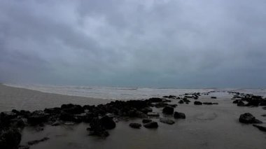 Kasvetli bir deniz manzarası engebeli bir kayalık kıyı şeridini geniş, uğursuz bulutlara karşı sergiliyor.