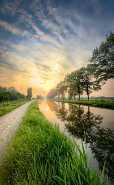 Görkemli bir kanal üzerinde sakin bir gün doğumu, yemyeşil ve doğa arasında çarpıcı yansımalar sergiliyor.