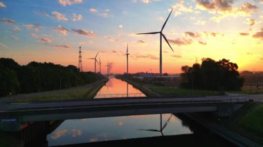 Nefes kesen bir günbatımı, sayısız rüzgar türbiniyle birlikte sakin suyu parlak bir şekilde yansıtıyor.
