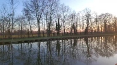 Güzel, sakin bir sahne. Ağaçları ve çarpıcı su yansımalarını canlı bir günbatımında sergiliyor.