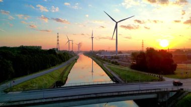 Gün batımında bir kanalın yanındaki rüzgar türbinlerinin nefes kesici görüntüsü yenilenebilir enerji ve doğa sergiliyor..
