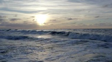 Büyüleyici bir okyanus batımı bulutlu gökyüzünün altındaki dalgaları kusursuz bir şekilde sergiliyor, doğa ve seyahat teması için ideal.