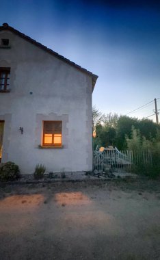 Bergnicourt, Rethel, Ardennes, Grand-Est, Fransa, 28 Ağustos 2025, Alacakaranlıkta konforlu ve kırsal bir ev doğanın ortasından yayılan sıcak bir parıltıyla güzelce tamamlanır.