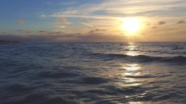 Güzel bir günbatımı, okyanus dalgaları üzerinde sıcak bir parıltı bırakır. Onları altın yansımalar ve sakin bir gökyüzüyle aydınlatır.