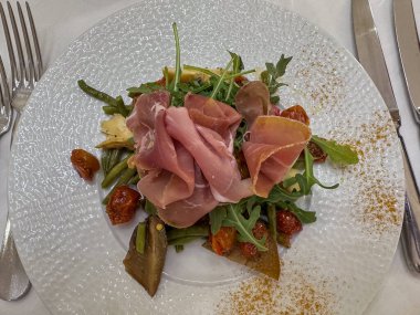 Canlı ve renkli bir salata tabağı bol jambon, taze yeşillikler ve vişneli domateslerle süslenmiş.