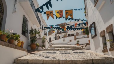 Low angle view of banners and buntings hanging between whitewashed houses over steps in Andalusia, Spain during sunny day clipart