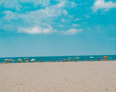 Uzaktan kumlu sahilde rahatlayan ve eğlenen insanların manzarası yaz boyunca mavi gökyüzünün altında güzel deniz manzarası ve ufuk manzarası.