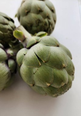 Beyaz arka planda enginarlar. Yiyecek olarak yetiştirilmiş devedikeni türünün yenilebilir tomurcukları..  