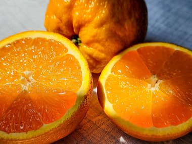 Beyaz keten bir masa örtüsü üzerinde tam meyve ve güneş ışığıyla aydınlatılmış sulu portakal. Yakın plan. Makro.