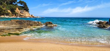 Dalgalar ve kayalarla kaplı bir deniz manzarası. Akdeniz kıyıları güneşli bir günde. Akdeniz ve kayalar. Kum kıyısı. Yaz günü. Costa Brava. İspanya. 