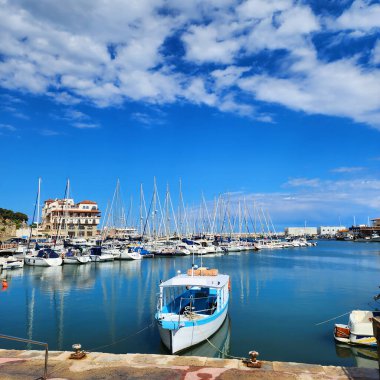 Tekne marinada demirlemiş. Arka planda liman ve yatları olan deniz manzarası. 