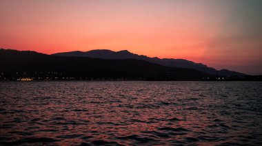 Turuncu-pembe gün batımına karşı deniz ve dağ silueti. Gün batımlı deniz manzarası.