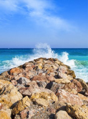 Seascape. Turquoise waves crashing on coastal rocks against blue sky with clouds. clipart