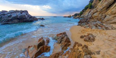 Sert kayalık kıyılar. Dalgalı denizde büyük taşlar ve kayalar. Yağmurdan sonra deniz manzarası.