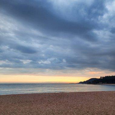 Yağmurdan sonra akşam deniz manzarası. Kumsal, deniz ve kayalar gün batımında. Akdeniz kıyısı.
