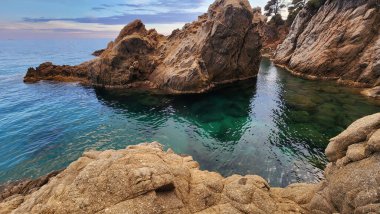 Sakin su yüzeyi ve kayaları olan deniz burnu. Turkuaz şeffaf su. Akdeniz kıyısında akşam.