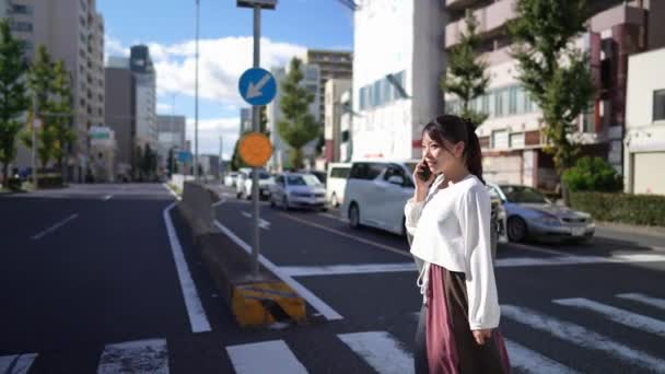 Młoda Japonka Spacerująca Podczas Rozmowy Smartfonie Wzdłuż Drogi Niedaleko Dzielnicy — Wideo stockowe