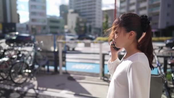 Wanita Muda Jepang Berjalan Sambil Berbicara Telepon Pintarnya Sepanjang Jalan — Stok Video