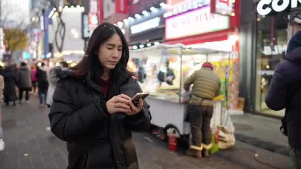 30代の韓国人男性が長髪で ソウル 明洞の通りで冬の雪を夜に観光する — ストック動画