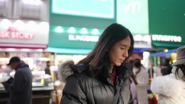 韩国首尔明东的一个寒冷的雪夜 一个30多岁的长发韩国男人在夜市里购买和吃小吃 — 图库视频影像