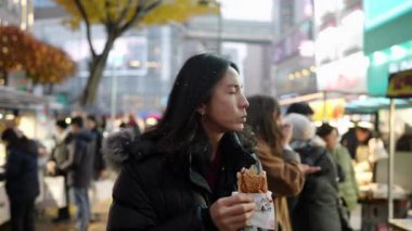 Myeong-dong, Seul, Güney Kore 'de soğuk bir gecede gece marketinden atıştırmalık alıp yiyen 30' lu yaşlarda uzun saçlı Koreli bir adam.