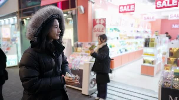 30代の長髪の韓国人男性が ソウル 韓国の雪の寒い夜に夜市を歩いているフードを着ています — ストック動画