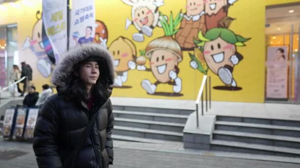 韩国首尔绵东市 一个30多岁 头戴头巾 头戴长发的韩国男人 在一个寒冷的雪夜里走在夜市 — 图库视频影像