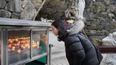 Myeong-dong, Seul, Güney Kore 'de soğuk bir kış günü kilisede tanrıça heykeline dua eden 30' lu yaşlarında uzun saçlı Koreli bir adamın yavaş çekim videosu.