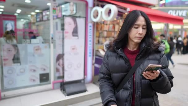 30代の韓国人男性のスローモーションビデオは ソウル 明洞の寒い冬にスマートフォンを操作しています — ストック動画