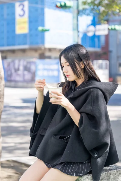 A young Taiwanese woman in her 20s eating street food tofu pudding around Zhongshan Station in Zhongshan District, Taipei City, Taiwan