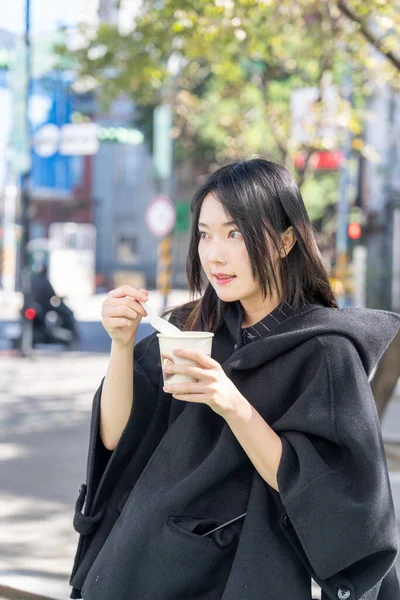 A young Taiwanese woman in her 20s eating street food tofu pudding around Zhongshan Station in Zhongshan District, Taipei City, Taiwan