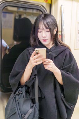 20 'li yaşlarda Tayvanlı genç bir üniversite öğrencisi akıllı telefonunu Taipei, Tayvan' da bir metro istasyonunda ya da trende kullanıyor.