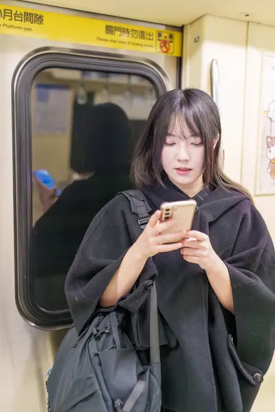 20 'li yaşlarda Tayvanlı genç bir üniversite öğrencisi akıllı telefonunu Taipei, Tayvan' da bir metro istasyonunda ya da trende kullanıyor.
