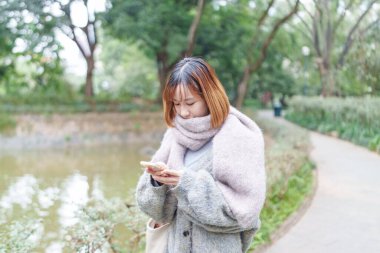 20 'li yaşlarda Çinli bir kadın kışın soğuk olan Hong Kong' da, Tsim Sha Tsui 'de bir parkta vakit geçiriyor.