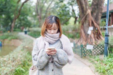 20 'li yaşlarda Çinli bir kadın kışın soğuk olan Hong Kong' da, Tsim Sha Tsui 'de bir parkta vakit geçiriyor.