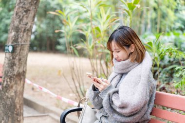 20 'li yaşlarda Çinli bir kadın kışın soğuk olan Hong Kong' da, Tsim Sha Tsui 'de bir parkta vakit geçiriyor.