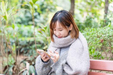 20 'li yaşlarda Çinli bir kadın kışın soğuk olan Hong Kong' da, Tsim Sha Tsui 'de bir parkta vakit geçiriyor.