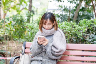 20 'li yaşlarda Çinli bir kadın kışın soğuk olan Hong Kong' da, Tsim Sha Tsui 'de bir parkta vakit geçiriyor.