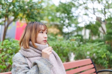 20 'li yaşlarda Çinli bir kadın kışın soğuk olan Hong Kong' da, Tsim Sha Tsui 'de bir parkta vakit geçiriyor.