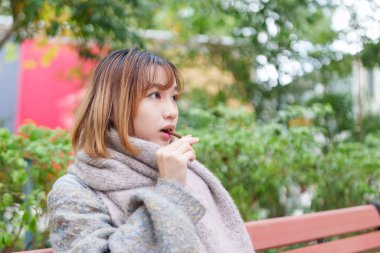 20 'li yaşlarda Çinli bir kadın kışın soğuk olan Hong Kong' da, Tsim Sha Tsui 'de bir parkta vakit geçiriyor.