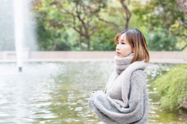 20 'li yaşlarda Çinli bir kadın kışın soğuk olan Hong Kong' da, Tsim Sha Tsui 'de bir parkta vakit geçiriyor.