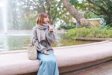 20 'li yaşlarda Çinli bir kadın kışın soğuk olan Hong Kong' da, Tsim Sha Tsui 'de bir parkta vakit geçiriyor.