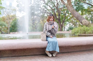 20 'li yaşlarda Çinli bir kadın kışın soğuk olan Hong Kong' da, Tsim Sha Tsui 'de bir parkta vakit geçiriyor.