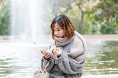 20 'li yaşlarda Çinli bir kadın kışın soğuk olan Hong Kong' da, Tsim Sha Tsui 'de bir parkta vakit geçiriyor.