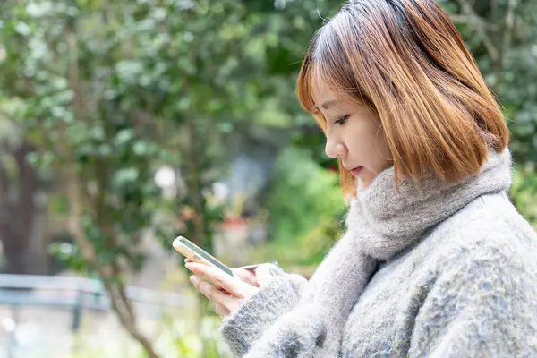 20 'li yaşlarda Çinli bir kadın kışın soğuk olan Hong Kong' da, Tsim Sha Tsui 'de bir parkta vakit geçiriyor.