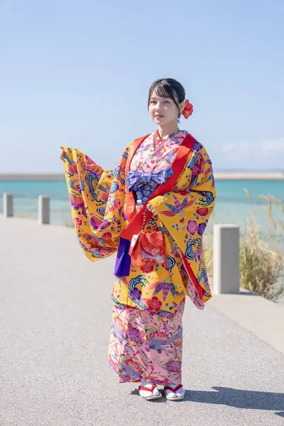 A young Japanese woman in her 20s in Ryukyu dress at a place with a view of the sea on Umikaji Terrace in Senaga, Tomigusuku City, Okinawa Prefecture