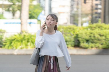 20 'li yaşlarda genç bir Japon kadın Aichi şehrinin Nagoya şehrinin sokaklarında akıllı bir telefonla konuşurken yürüyor.